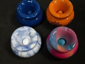 Cuatro ceniceros de silicona de diferentes colores dispuestos sobre una superficie negra: azul, naranja, marmolado azul y blanco, y uno multicolor en tonos rosa, azul y morado, vistos desde arriba.